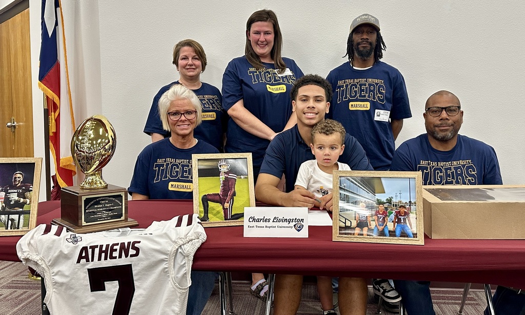 Teen boy seated behind table surrounded by family members.