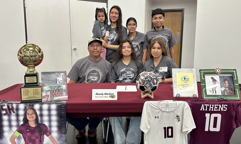 Teen girl seated behind table surrounded by family members.
