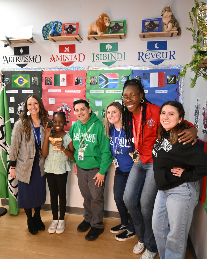 student smiles with trophy alongside teachers