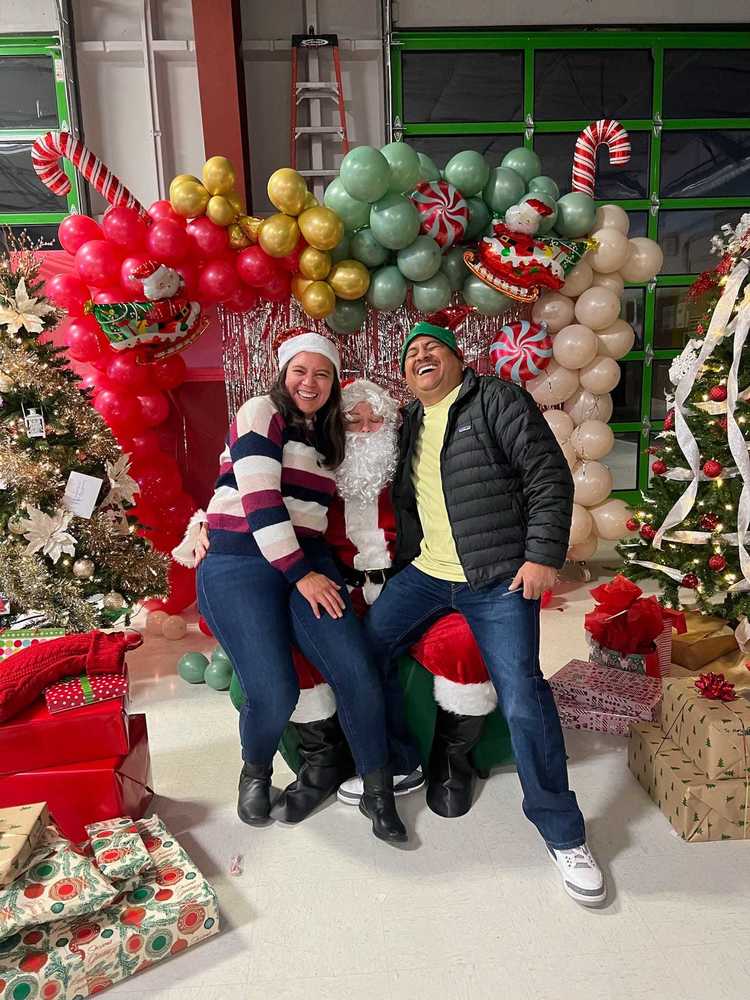 people sit on santa's lap and laugh, surrounded by balloons and presents