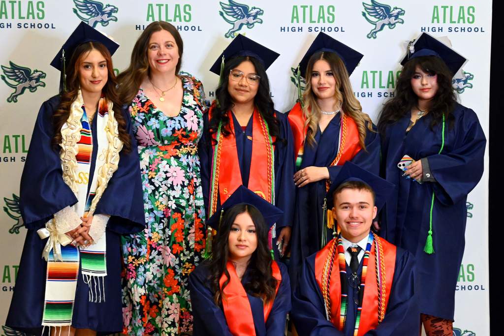 students smile in caps and gowns with teacher