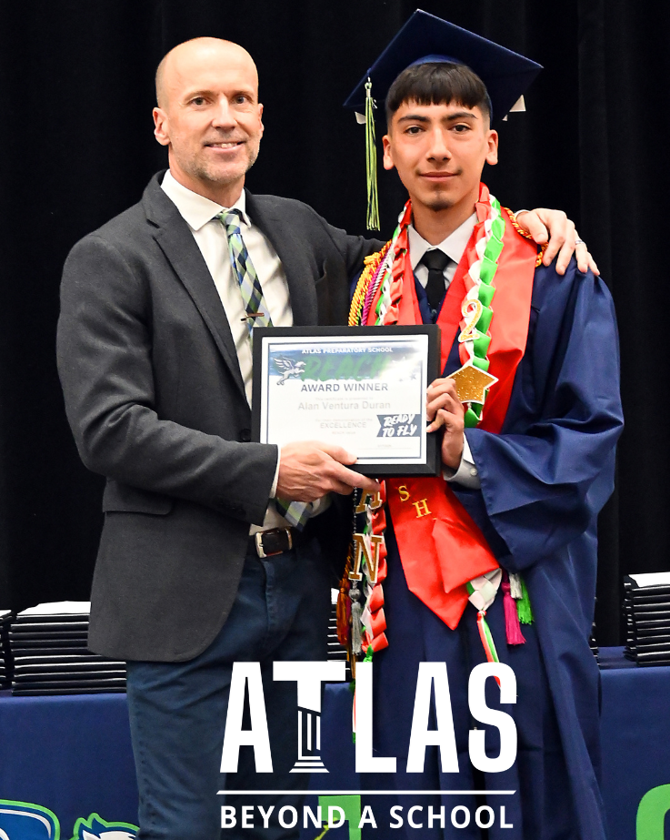 student in cap and gown posts with teacher and award