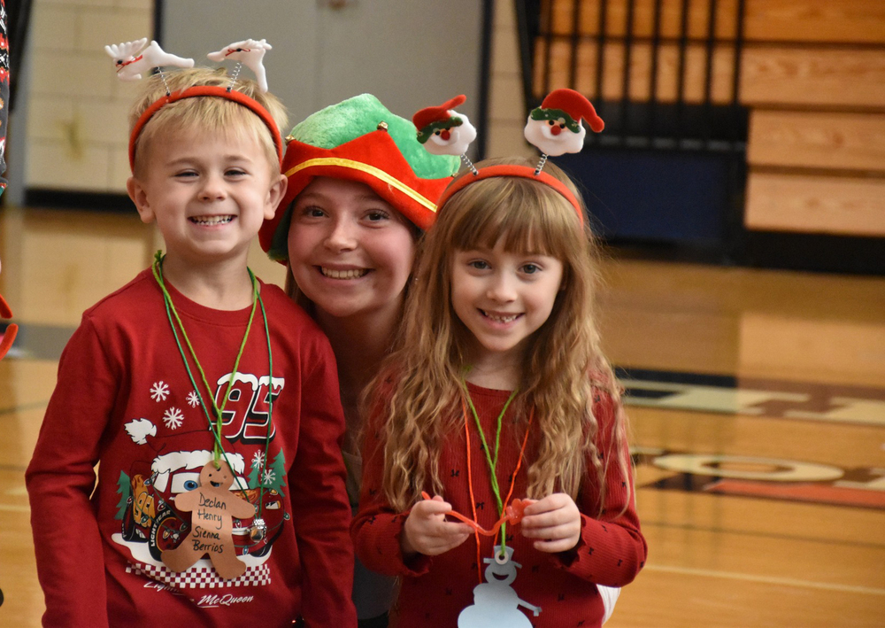 Kindergarteners Declan Henry, left, and Scarlett Galese, right, take a break from the many fun activities of Elf Day to pose for a photo with their ‘elf,’ senior Sienna Berrios, center.