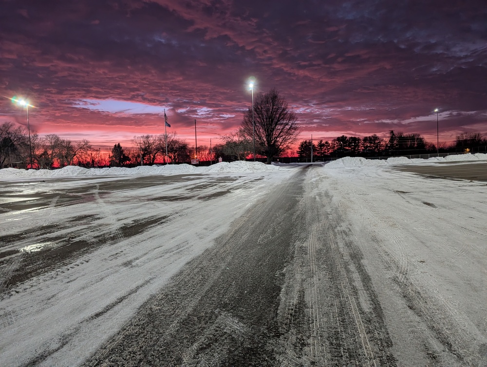An empty parking lot in winter at sunset with light poles shining in the distance.