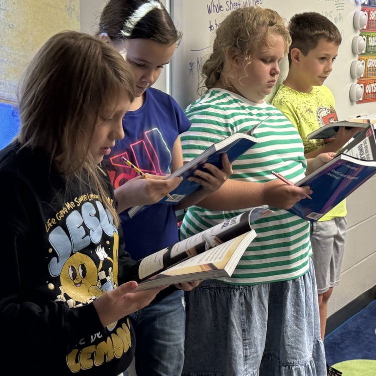 Four fourth graders standing with their ELA books in hand reading their part of the play. 