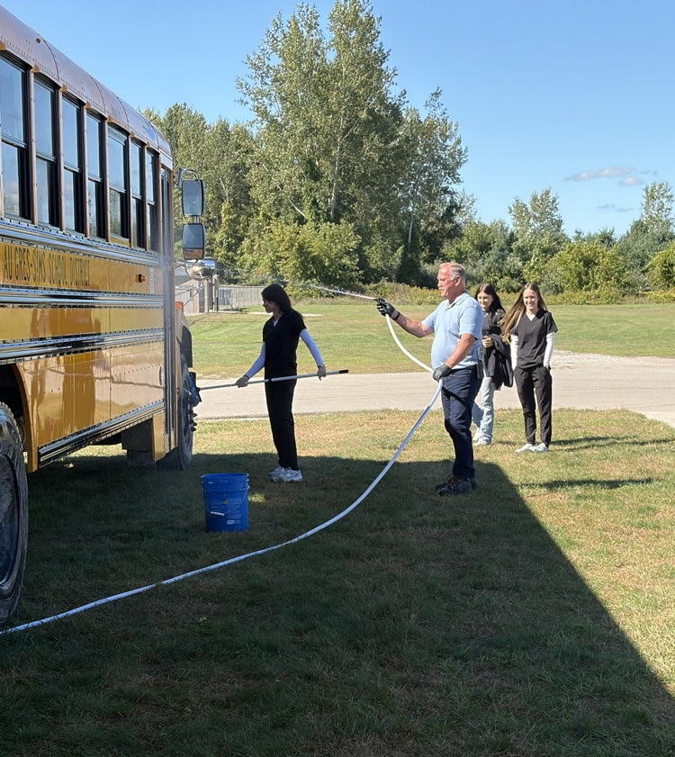 three students help a staff member wash a bus