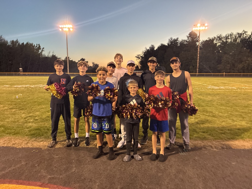 A group of boys standing in front of a football field holding cheerleading pom poms.