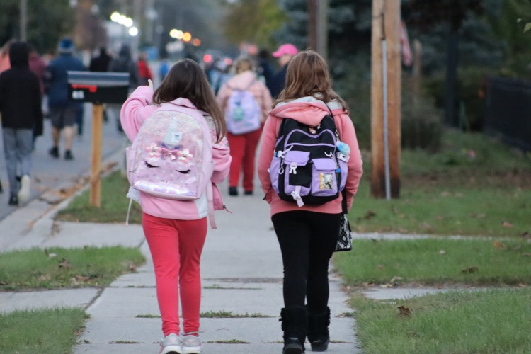 two girls walking on sidewalk 