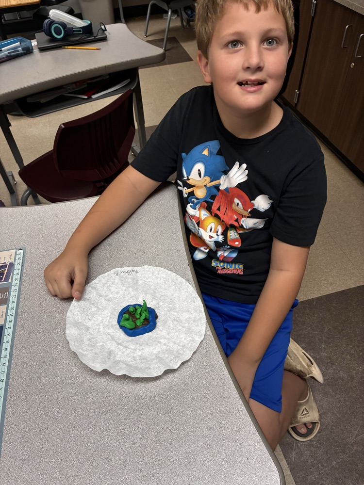 a boy holding clay models of landforms. 