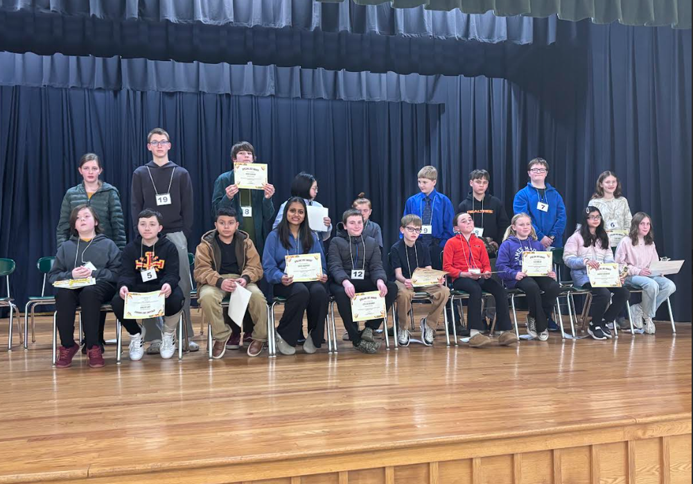 ACPS Spelling Bee participants lined up on stage holding up certificates