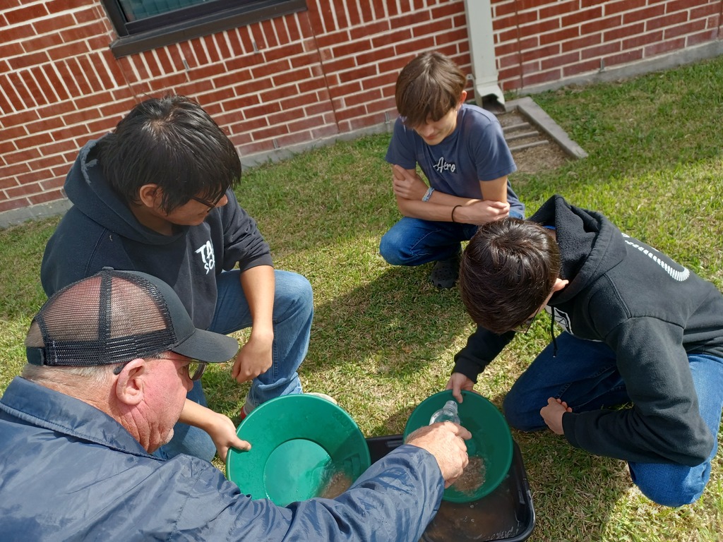 Students and a teacher use pans to find gold.