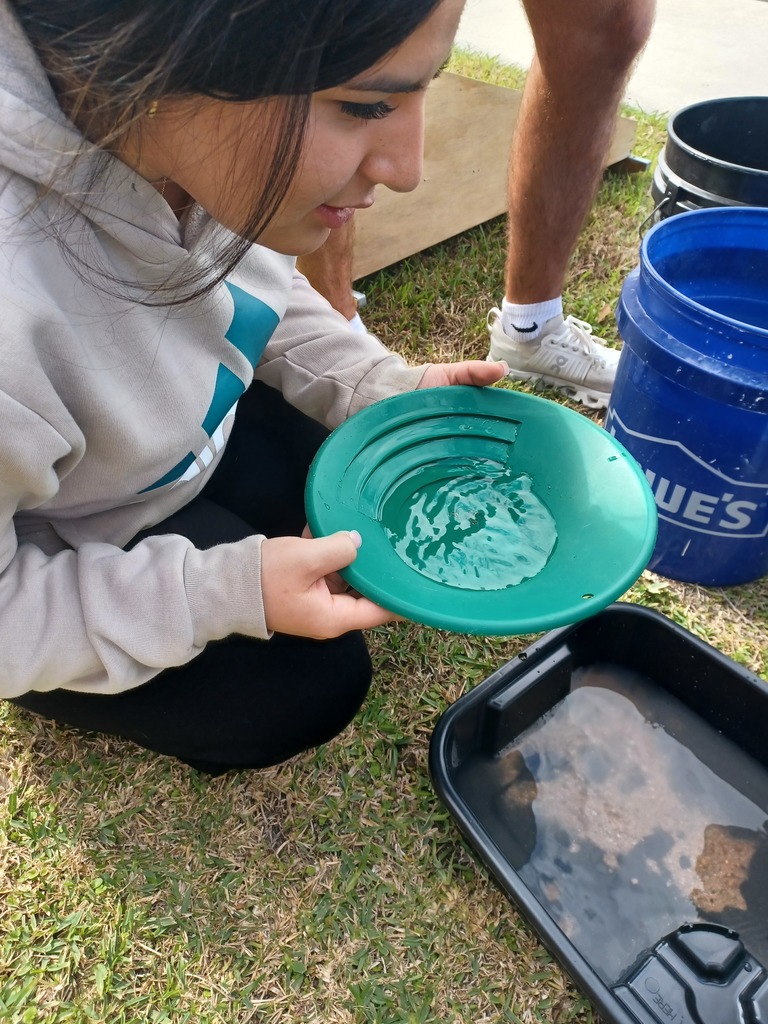A student looks in her pan to find flakes of gold.
