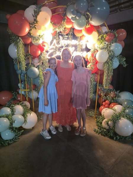 Mrs. Faith Steward Davison smiling at the camera with two students, balloons in the background.