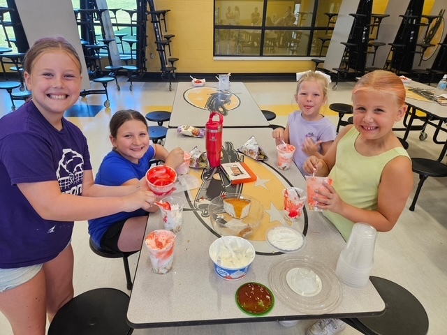 Group of four students adding whipped topping to dessert. 