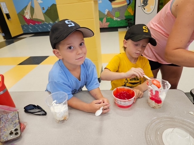 Students in ball caps making dessert. 