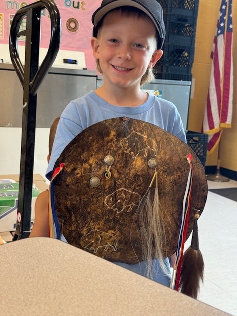 Male student in ball cap holding artifact. 
