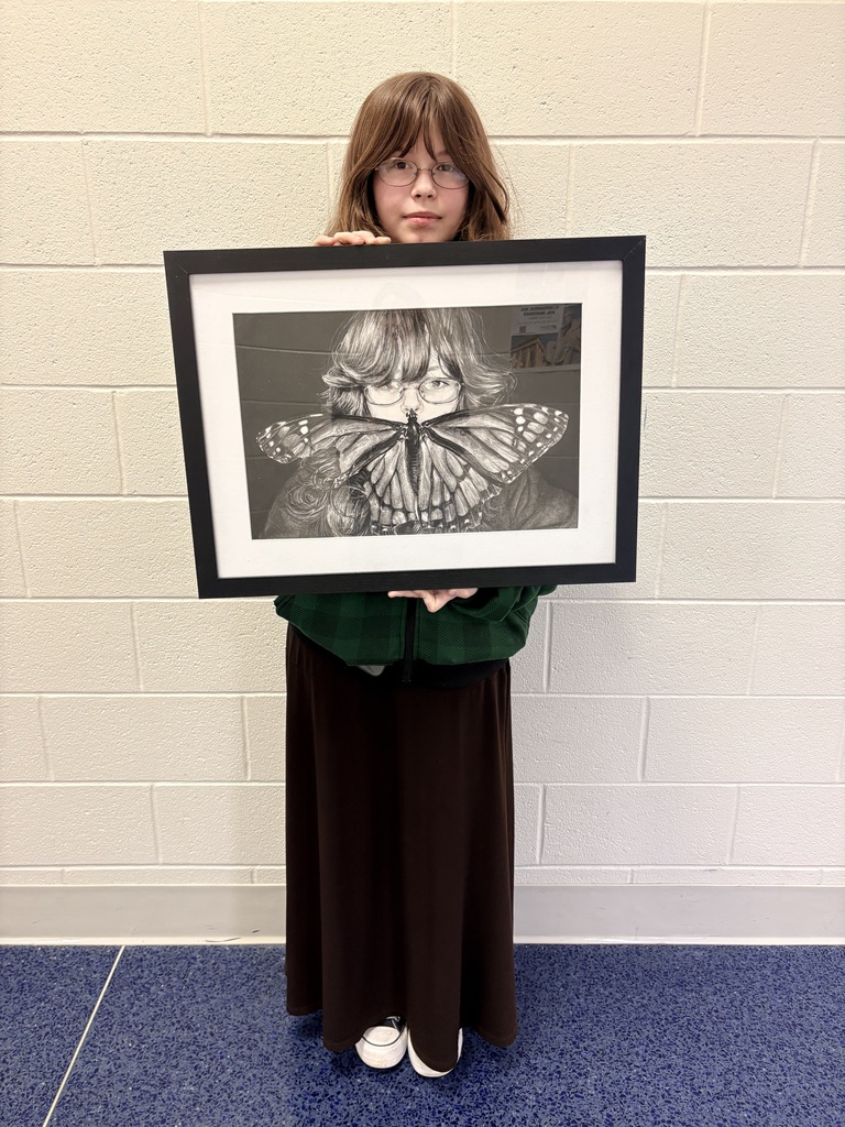 Ayersville student Olyvia stands proudly holding her framed award-winning artwork, 'The Feeble Mind Gone Mute.' The piece is a highly detailed black-and-white drawing featuring a portrait of a person partially obscured by a large, intricate monarch butterfly.