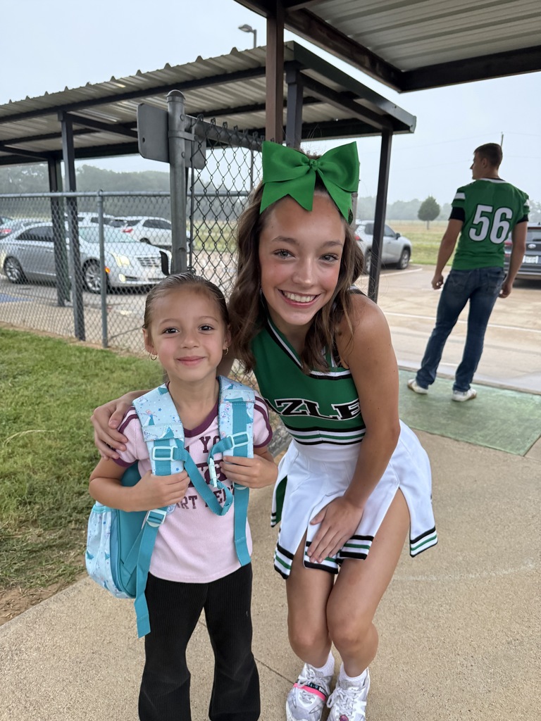 little girl wearing backpack standing with high school cheerleader