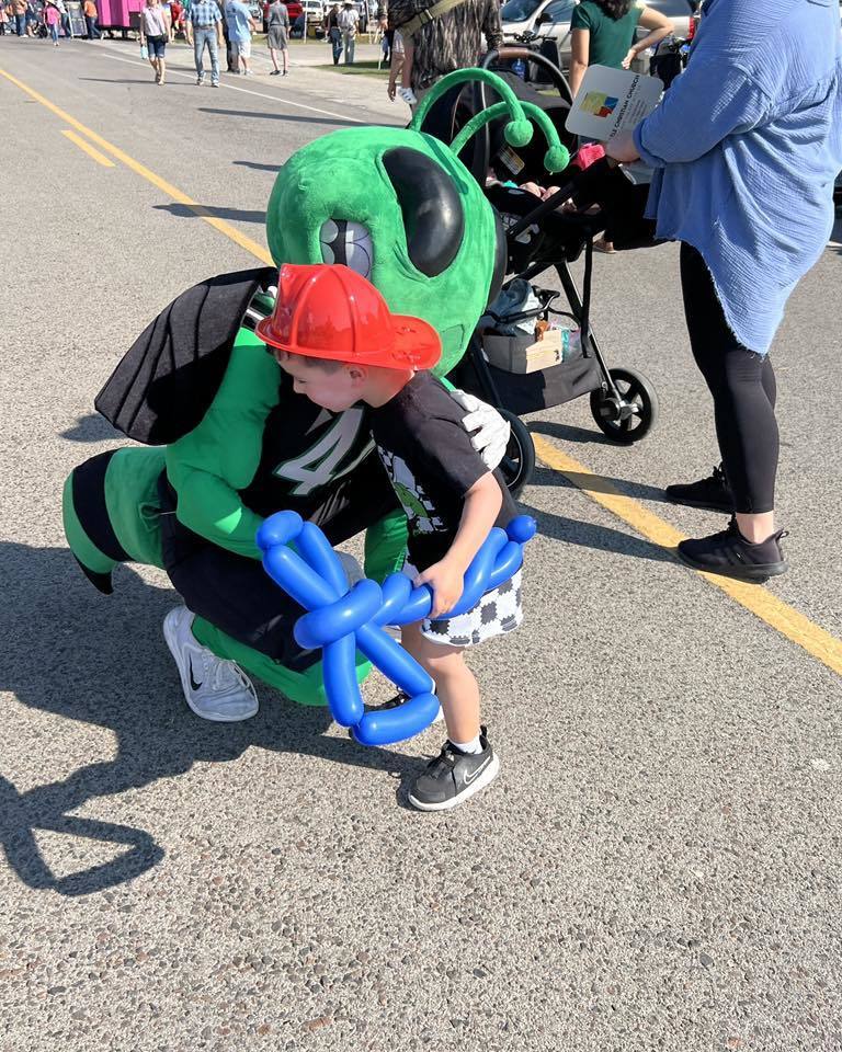 Buzzy bending down hugging little boy wearing red fireman hat