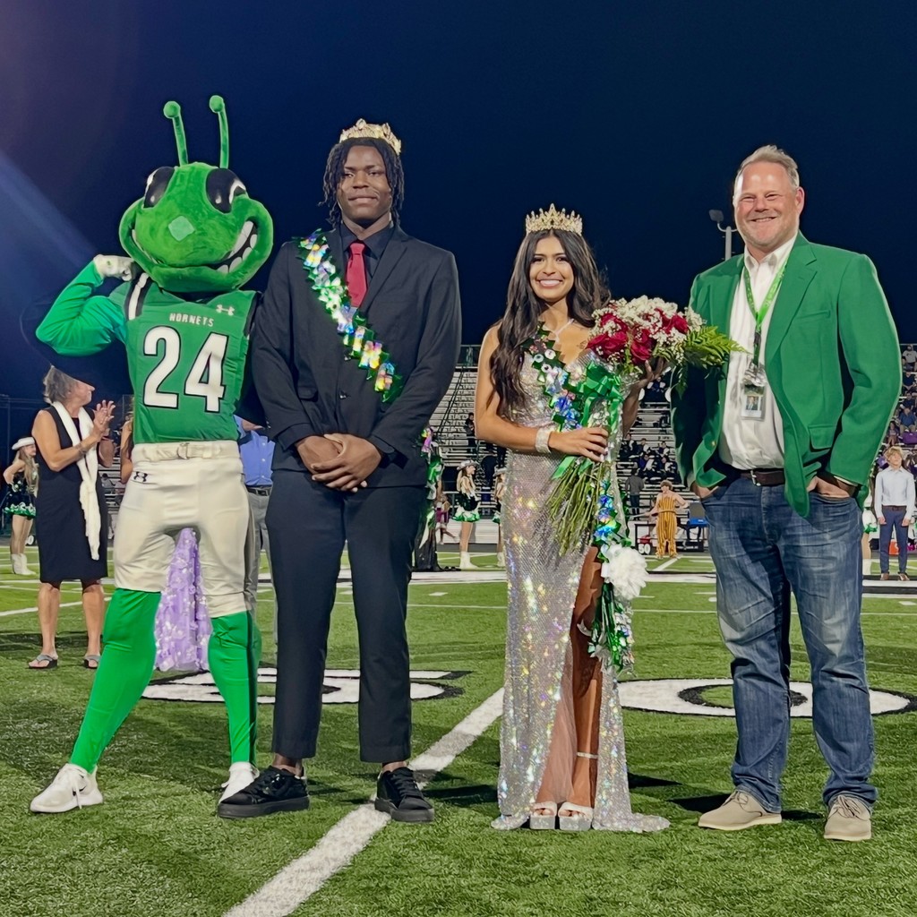 Buzzy, homecoming king & queen, and principal Driver standing on football field