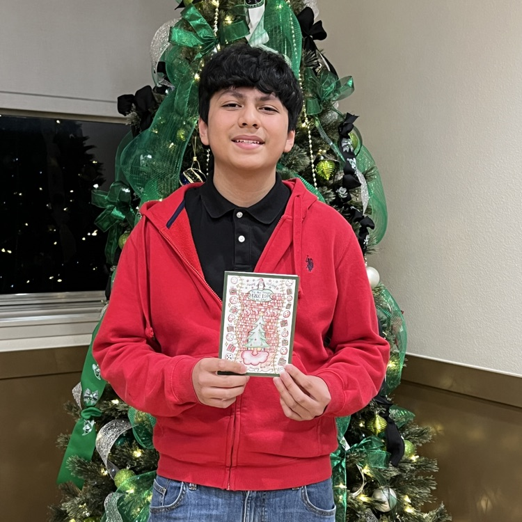junior high boy standing in front of Christmas tree holding card