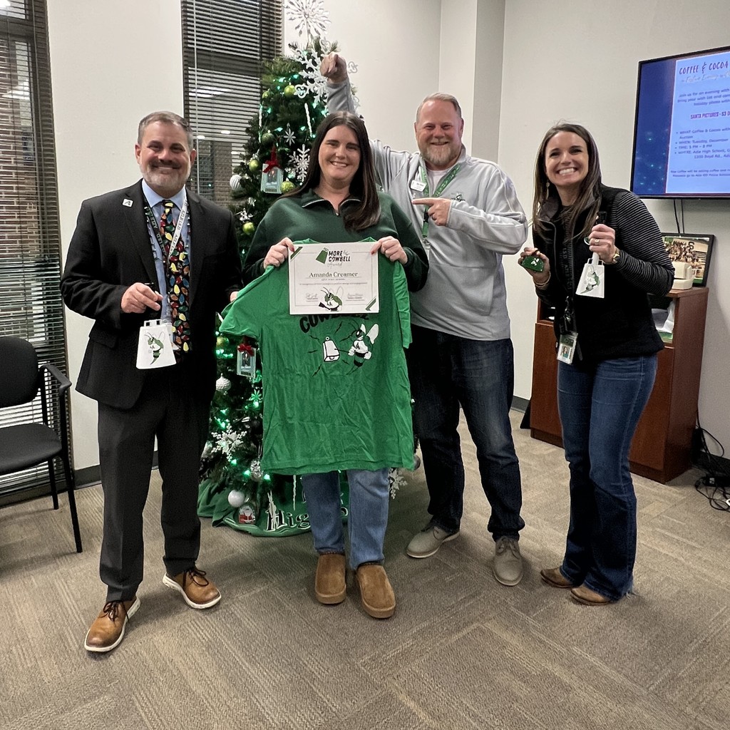 Superintendent Smith, Amanda Creamer (holding shirt & certificate), Mr. Driver, and Jessica Hanson standing in front of Christmas tree