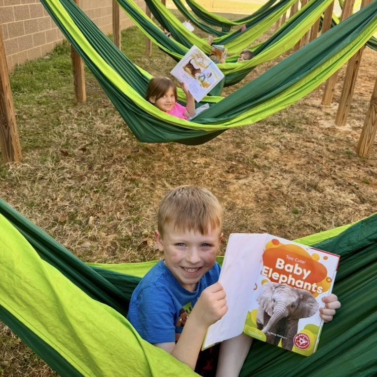 elementary students holding books, sitting in green and yellow reading hammocks