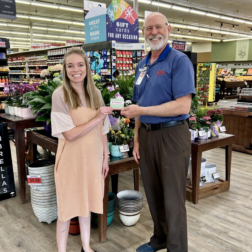 lady and man holding Brookshire's gift card with flowers and grocery isles in the background