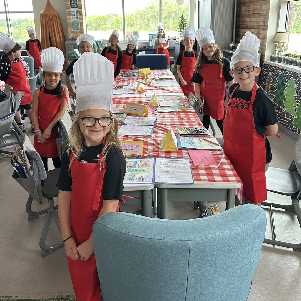 group of elementary students wearing chef hats and red aprons standing around a table