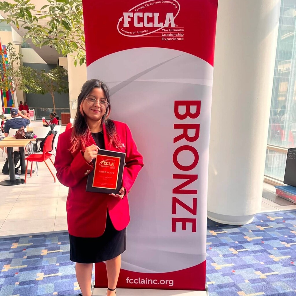 girl wearing red jacket, holding award and standing next to "FCCLA Bronze" banner