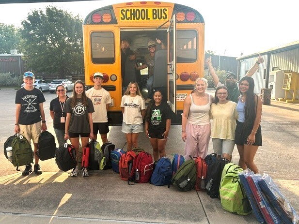group of high school students standing in front of bus with backpacks