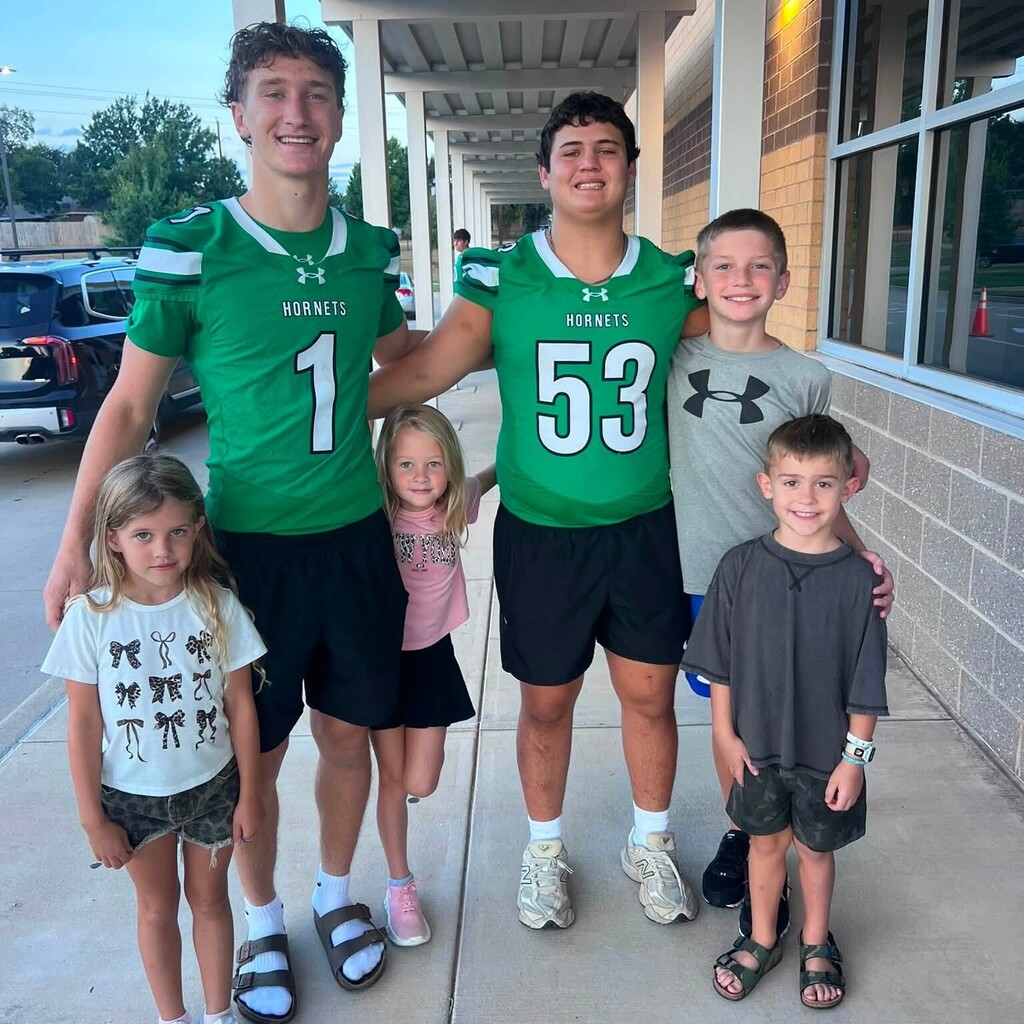two high school football players wearing green jerseys standing with 4 elementary students