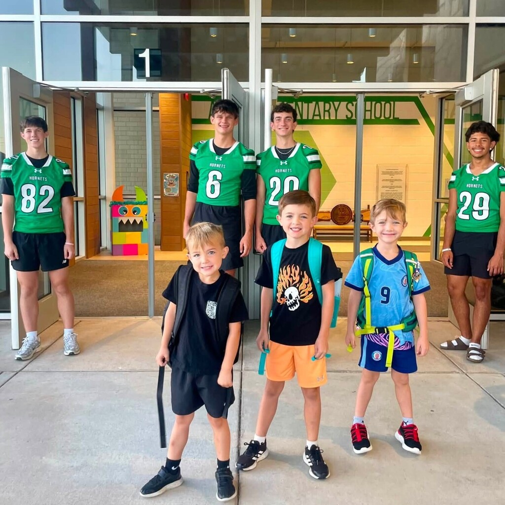 4 football players wearing green jerseys with three elementary boys standing outside school doors