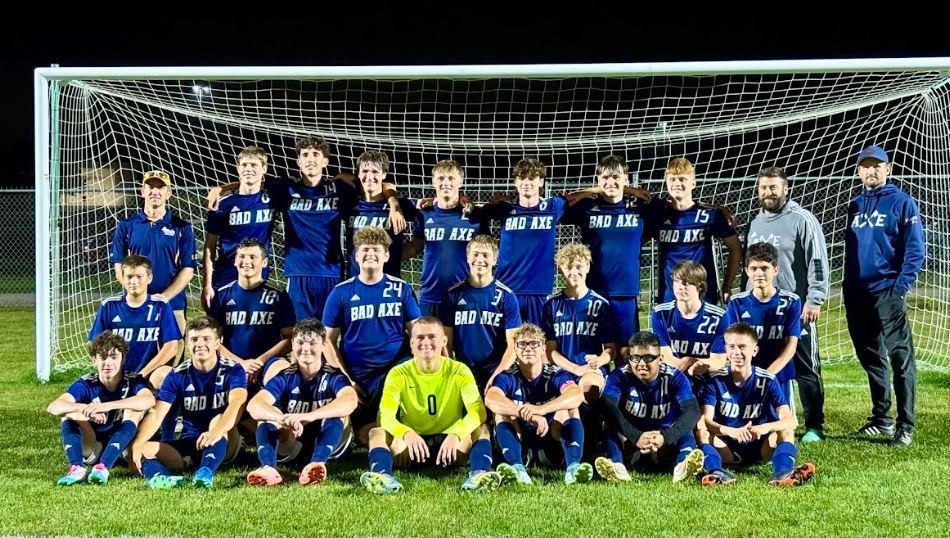 Bad Axe Boys Varsity Soccer team in blue jerseys sitting in front of the soccer net at night.