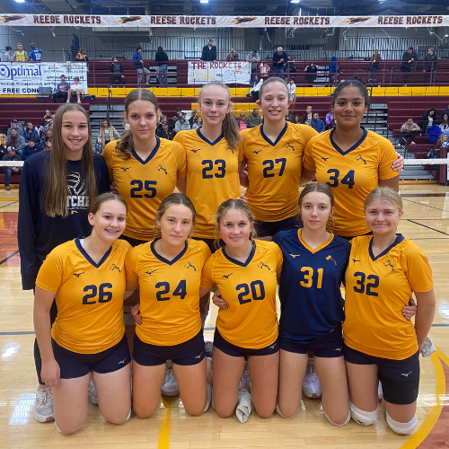 Bad Axe JV Volleyball Team wearing yellow jerseys, libero in navy jersey in a gymnasium.