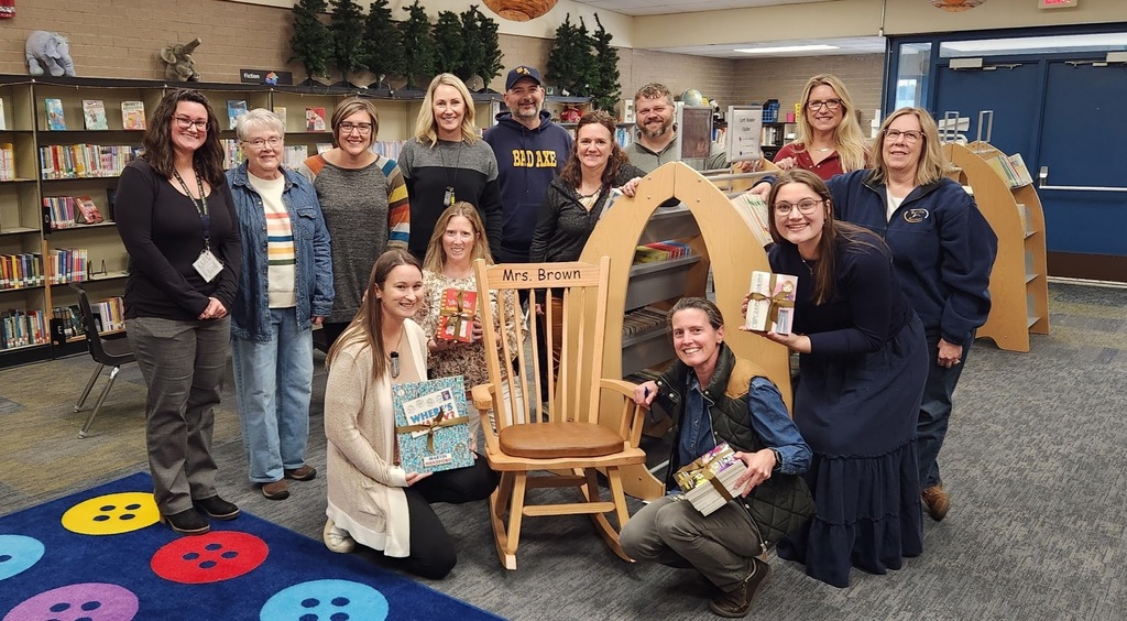 Bad Axe Elementary Staff & Teachers pose next to the rocking chair and books donated by Larry Brown & Family in memory of Kim Brown.