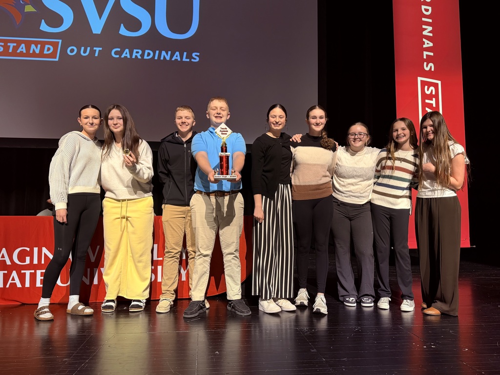 Bad Axe students stand on stage with the trophy from the Academic Games.