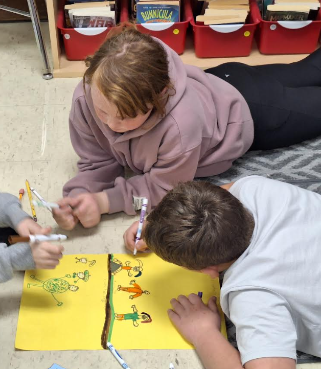 Two students drawing while laying on the floor.,