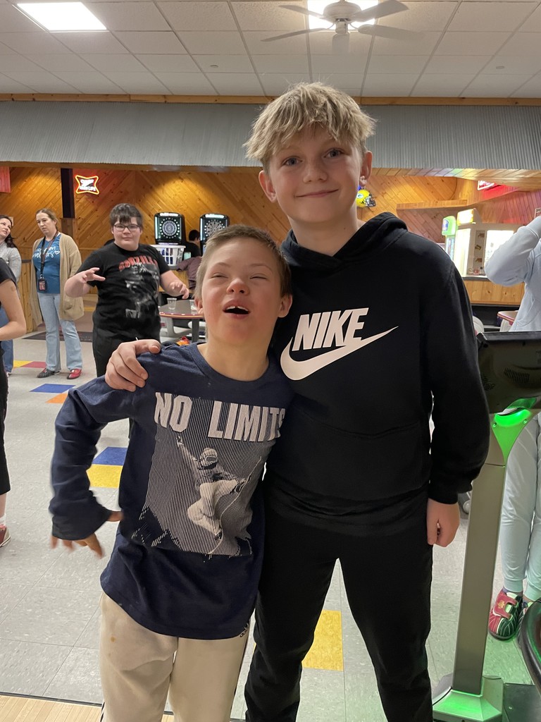 Two boys at the bowling alley standing by the lanes.
