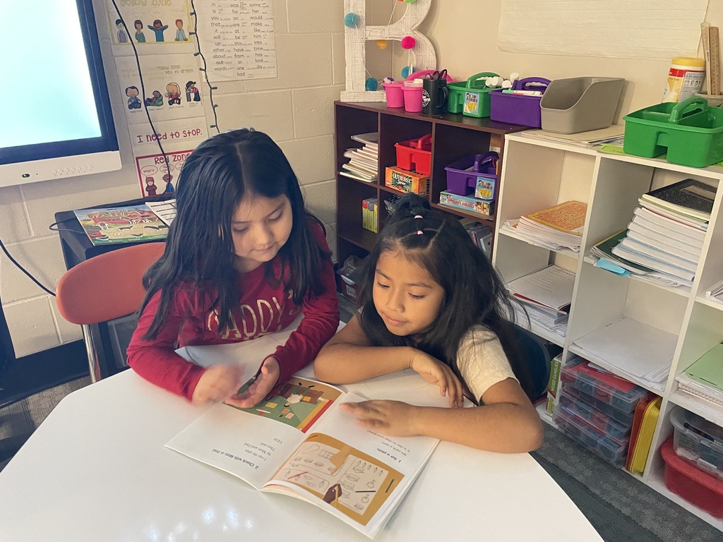 Two girls sitting at a table reading.