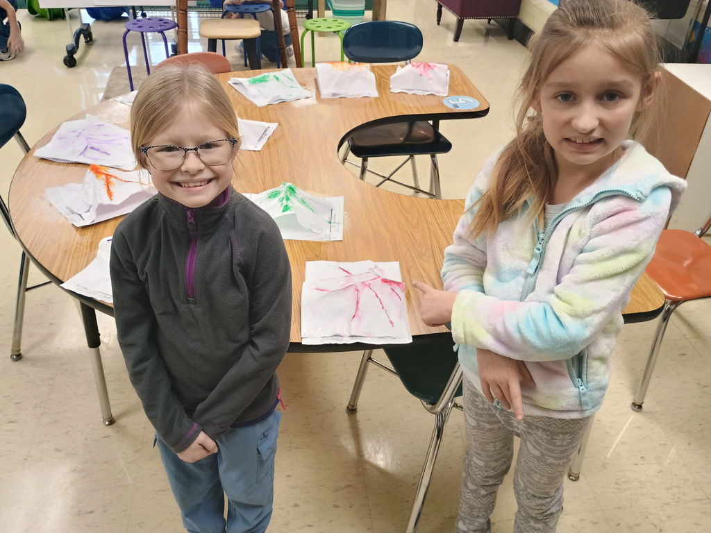 Students standing by a desk with all the projects.
