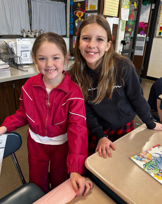 Two young girls smiling at their desks.