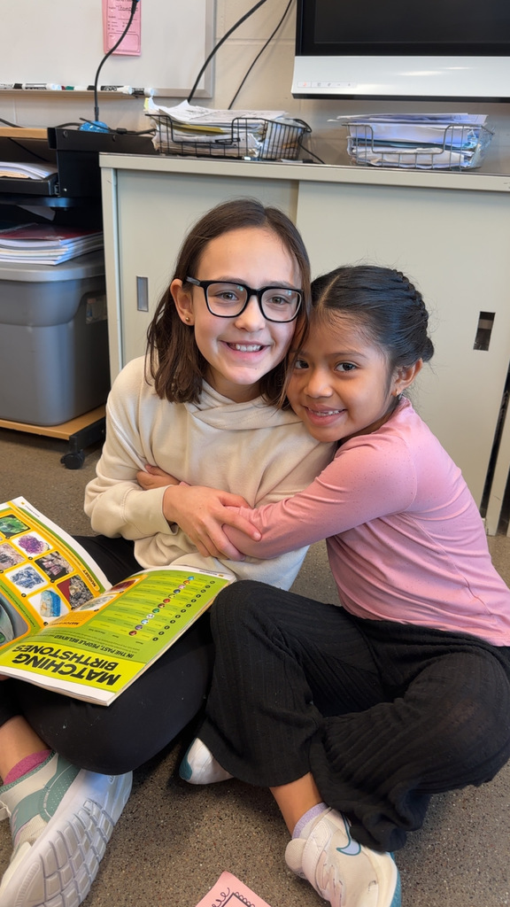 5th and 1st grade students hugging.