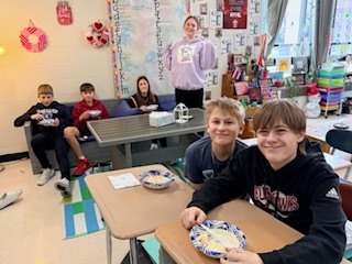 Students sitting on a couch, standing and sitting at their desk eating ice cream.