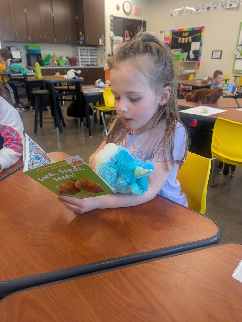 A little girl sitting at her desk with a book and stuffed animal.