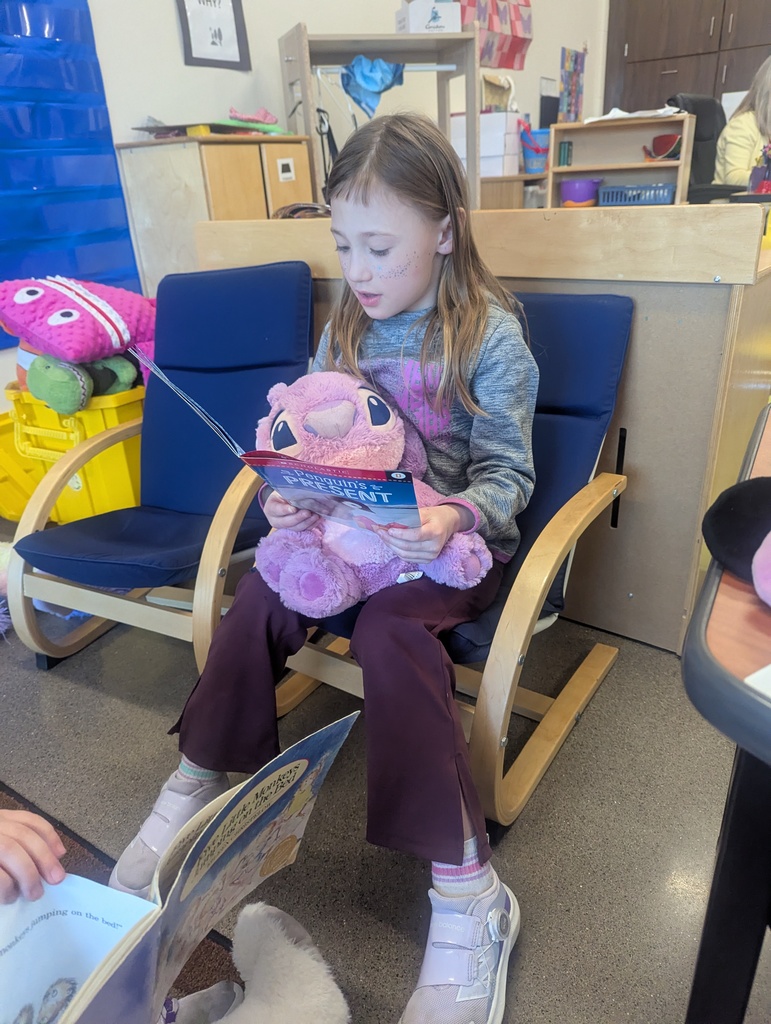 A little girl reading while holding her stuffed animal