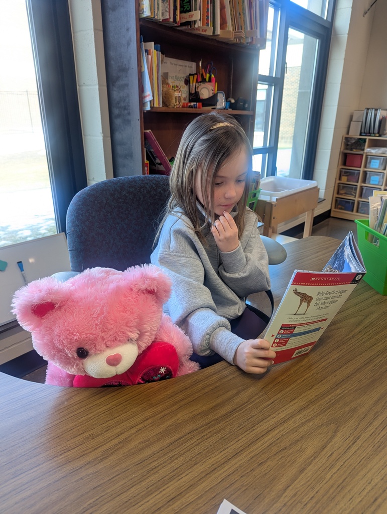A little girl looking at a book with her stuffed bear.
