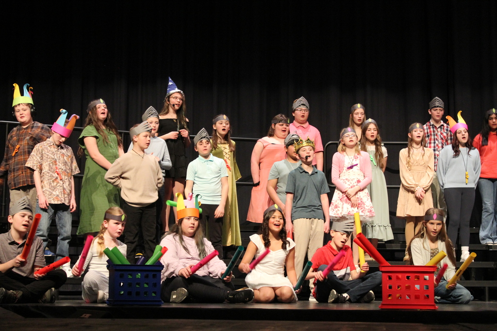 A large group photo of students on stage singing.