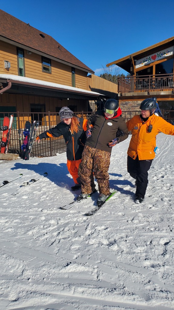 Two instructors helping a student on skis.