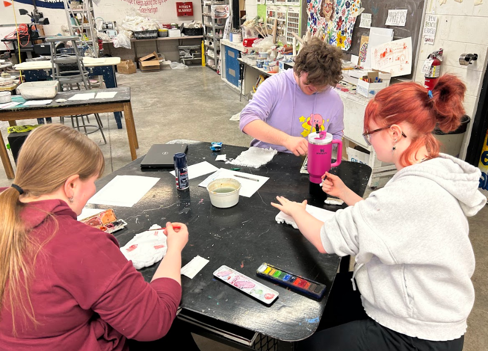 Three students at a table working on projects.